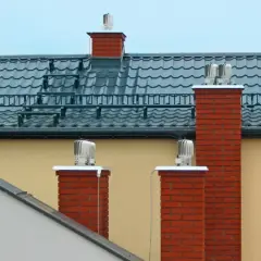 Dwa ceglane kominy z obrotowymi nasadami zapewniają sprawną wentylację w domu.