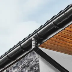 Nowoczesny system odprowadzenia wody z rynny, wykonany z czarnego tworzywa, skutecznie chroni elewację domu.