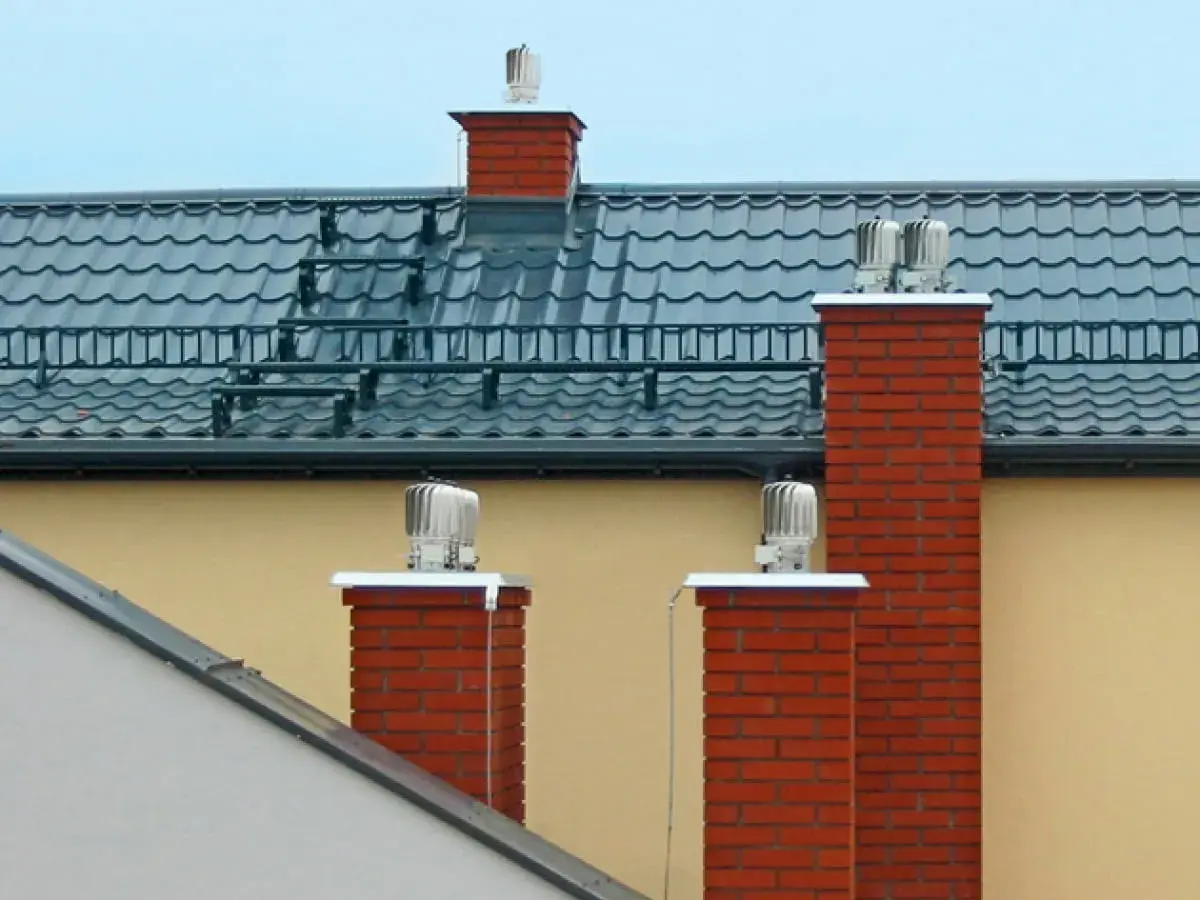 Dwa ceglane kominy z obrotowymi nasadami zapewniają sprawną wentylację w domu.
