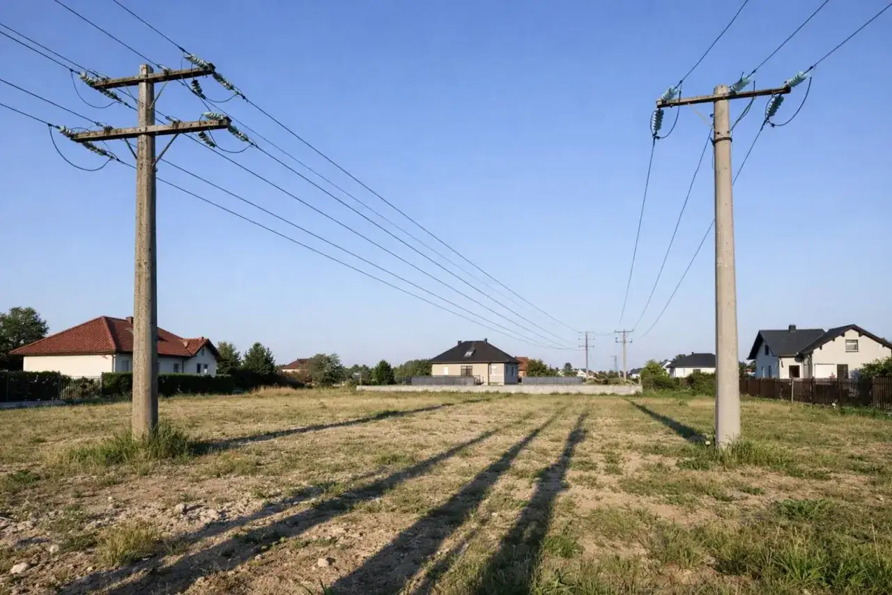 Działka z domami w tle, nad którą biegną linie wysokiego napięcia 110 kV. Ważne zachowanie bezpieczna odległość od linii wysokiego napięcia 110 kv.